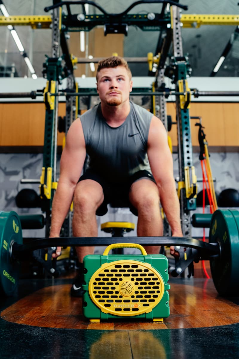 A lifestyle photo of a man in a gym setting with exercise equipment and weights. #speaker-color_green-yellow-gameday-series
