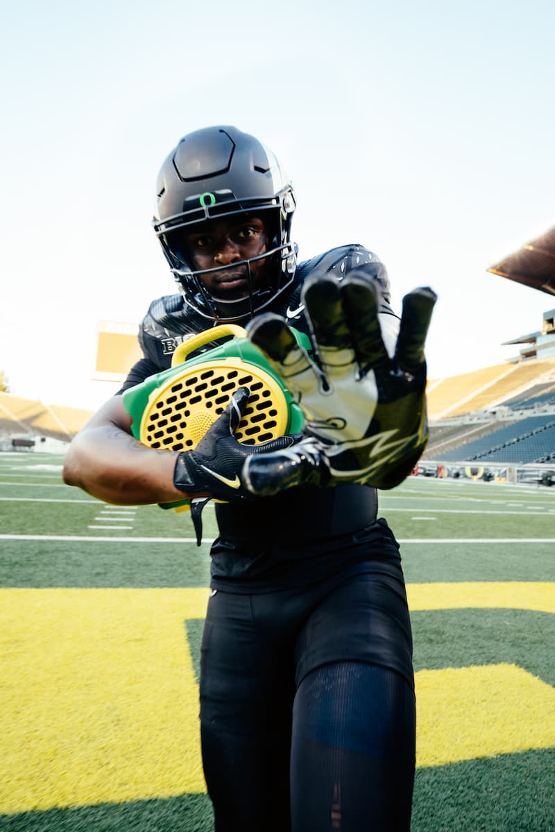 A lifestyle photo of a person in football gear holding a football on a field #speaker-color_green-yellow-gameday-series