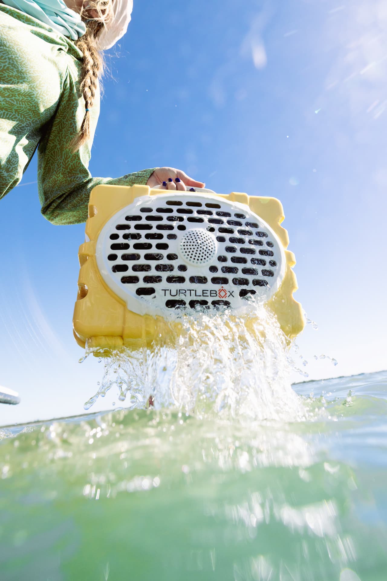 A lifestyle of a person holding a yellow Turtlebox device above water with a clear blue sky in the background #base-color_fighting-lady-yellow
