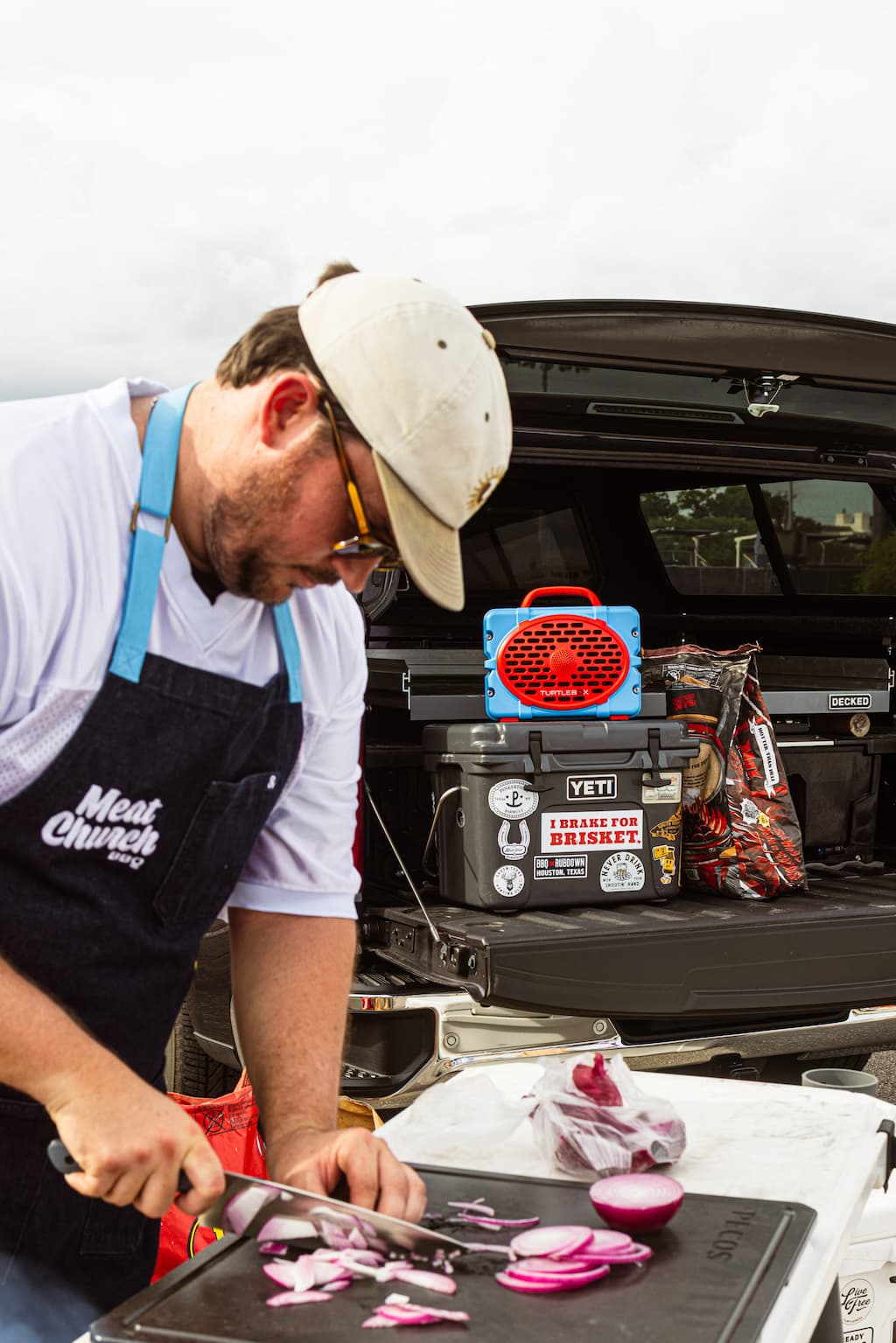 A lifestyle photo of a man cutting onions in slices with a Turtlebox Powder Blue & Red in the background. #speaker-color_powder-blue-red-gameday-series