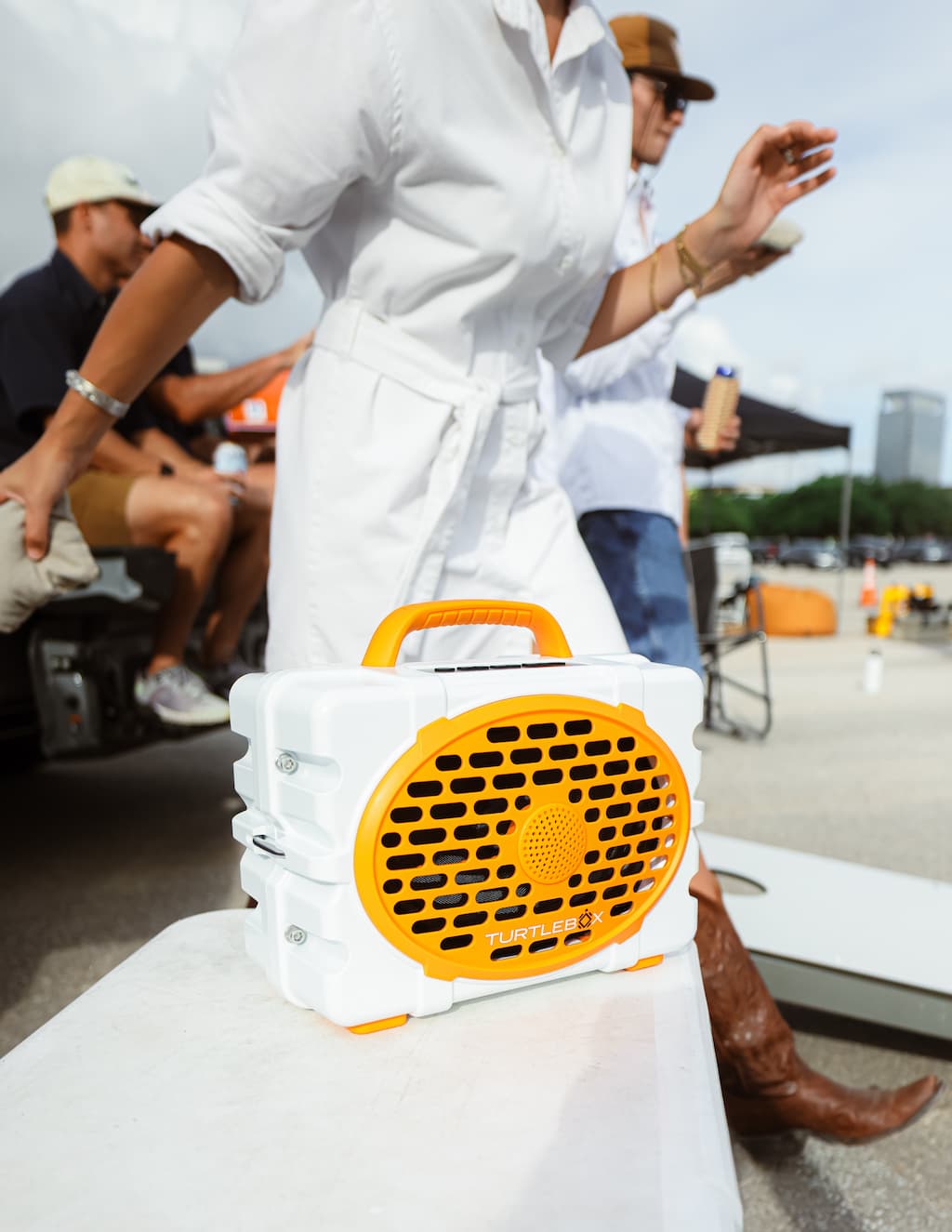 A lifestyle photo of a person holding a white and orange Turtlebox with people in the background #speaker-color_white-orange-gameday-series