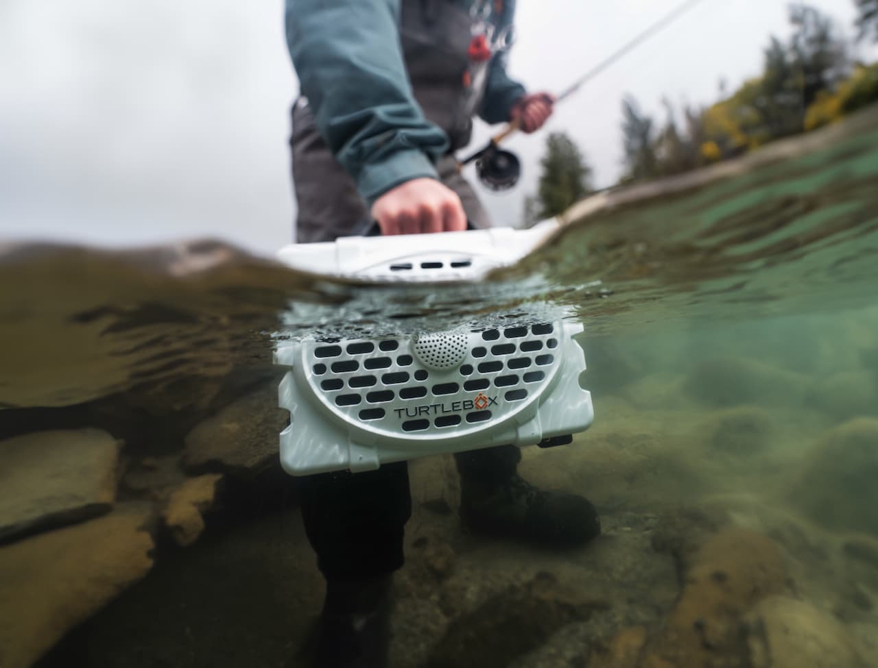 A lifestyle photo of a fisherman put his Turtlebox under water. #speaker-color_white