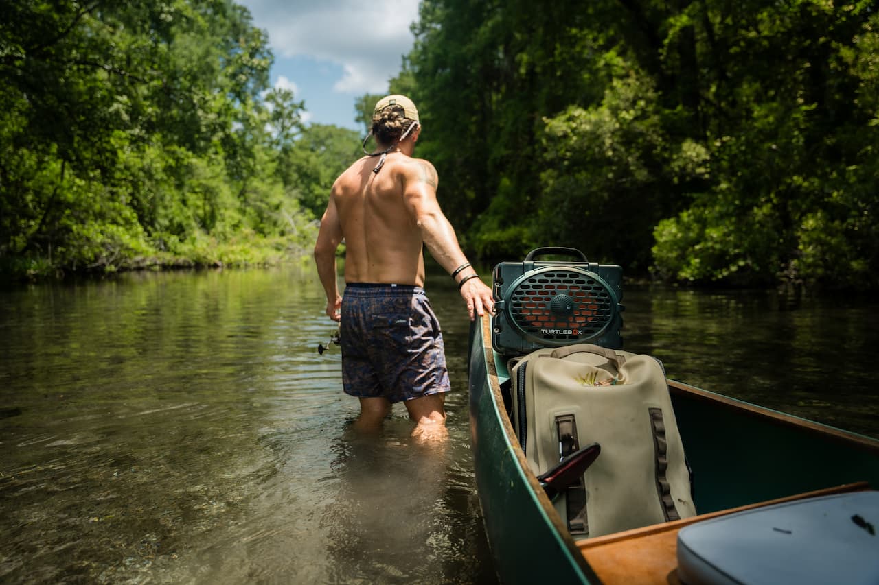 A lifestyle photo of a man in a river pulling his boat with a Turtlebox Original speaker in green attached to the boat #speaker-color_green